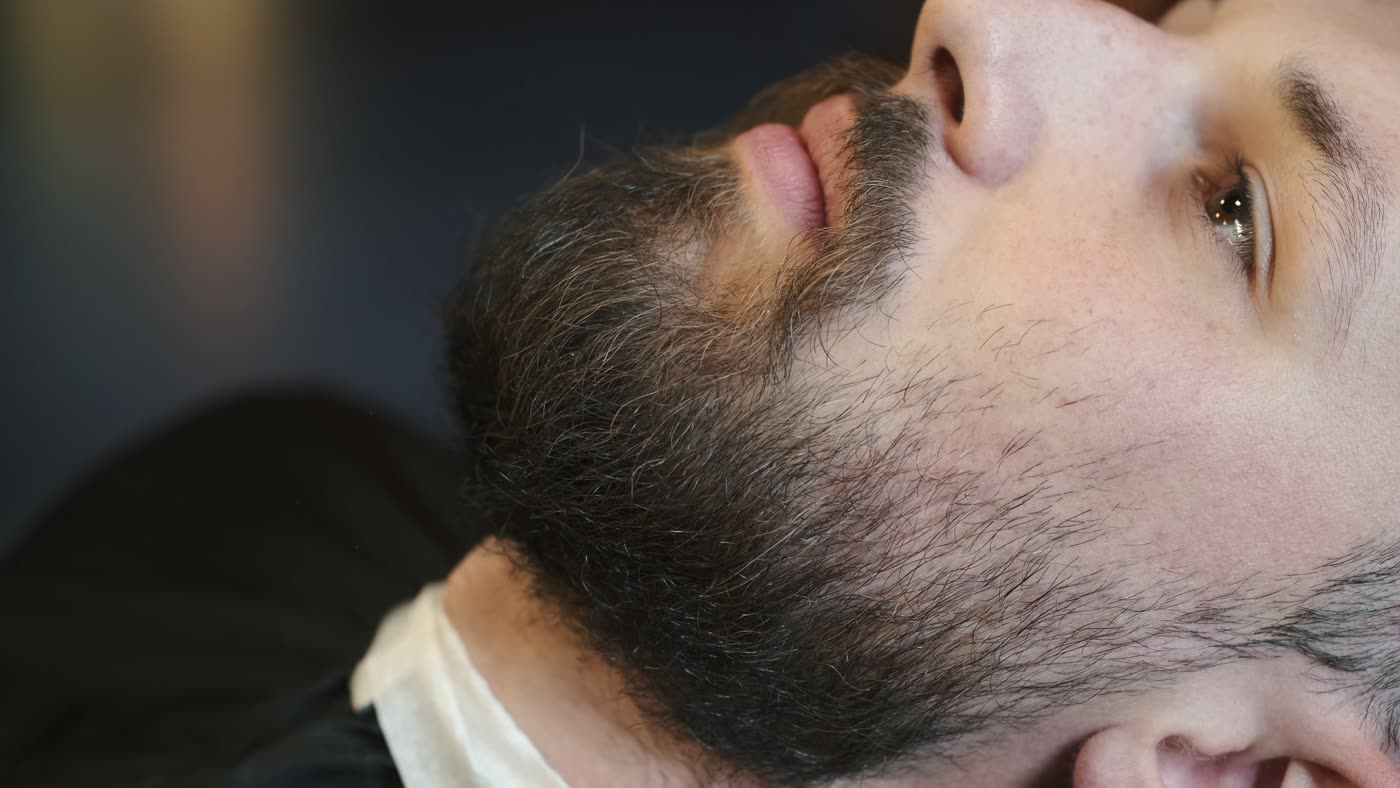 Cliente deitado enquanto o barbeiro trabalha a barba com pente e máquina